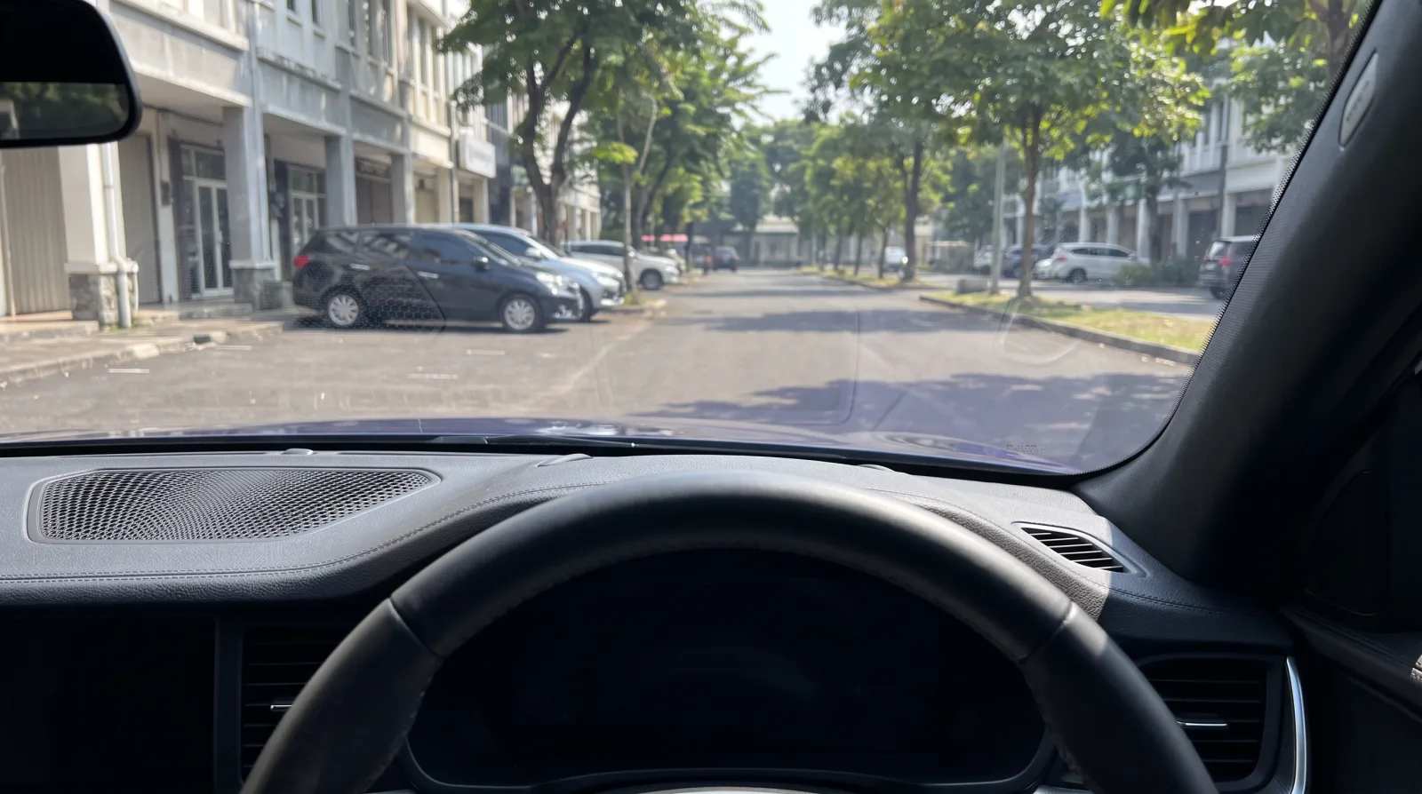 Mobil dan jalan yang sama setelah NanoShade dipasang, pandangan lewat kaca depan tajam dan jernih sampai ke daun di pohon, dashboard kembali gelap, dan warnanya utuh
