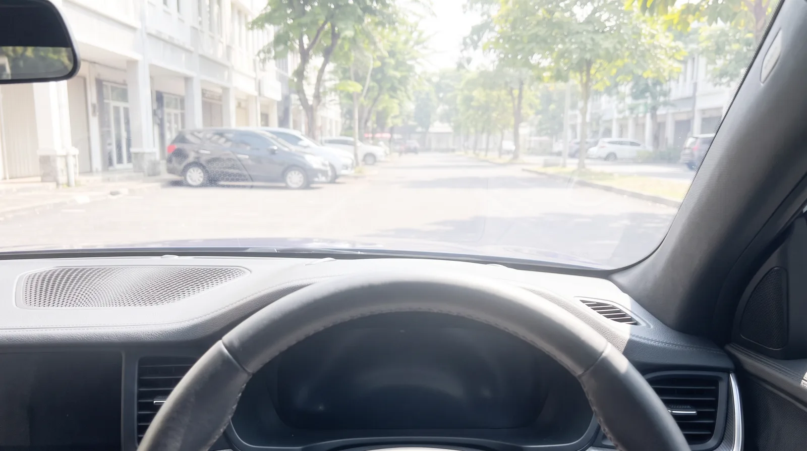 Mobil terparkir pukul dua siang tanpa film, jalan di balik kaca depan memutih oleh kabut cahaya, silau menyapu dashboard, dan warna pohon serta mobil yang terparkir tampak pudar