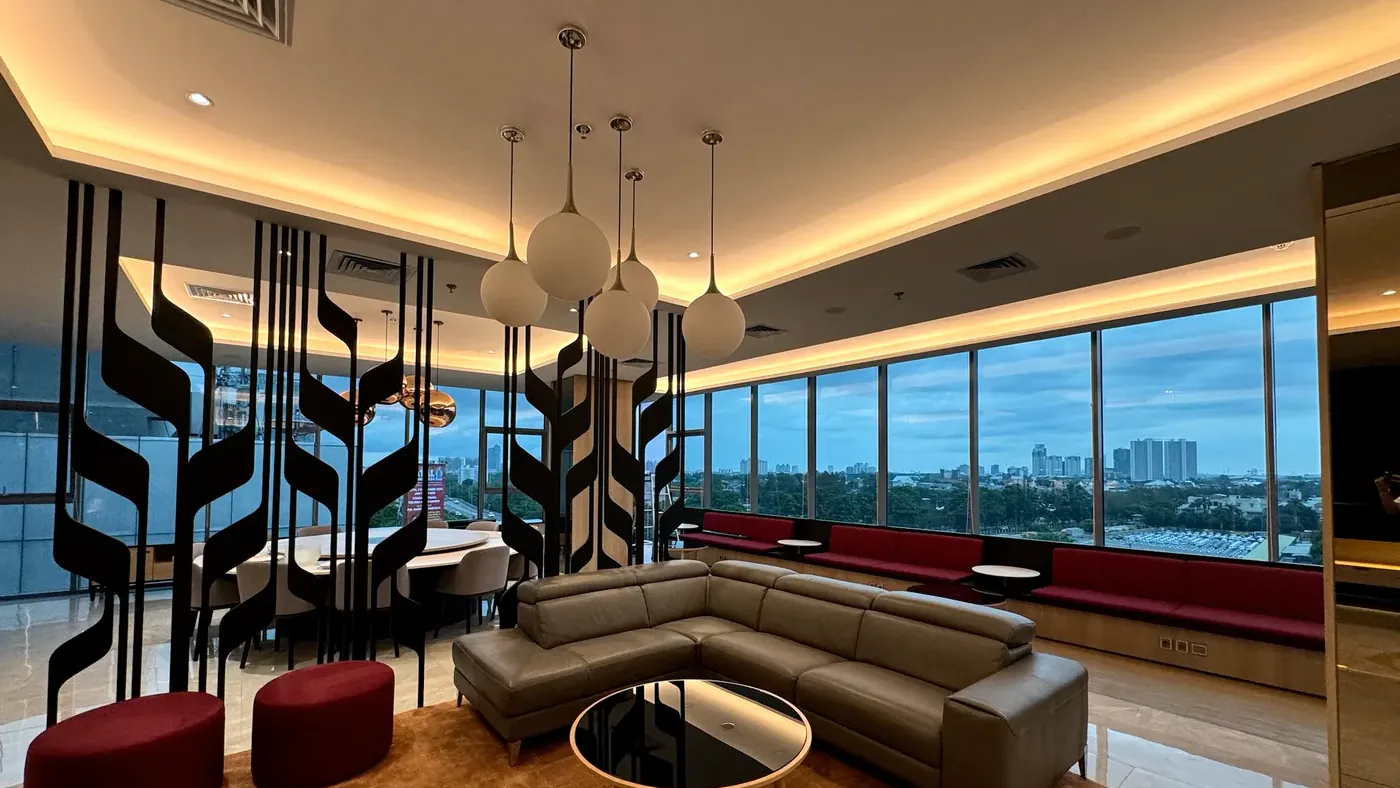 Pemasangan NanoShade yang sudah selesai, dinding kaca dengan film terpasang di lounge kantor di Jakarta saat senja, dengan kota terlihat melaluinya