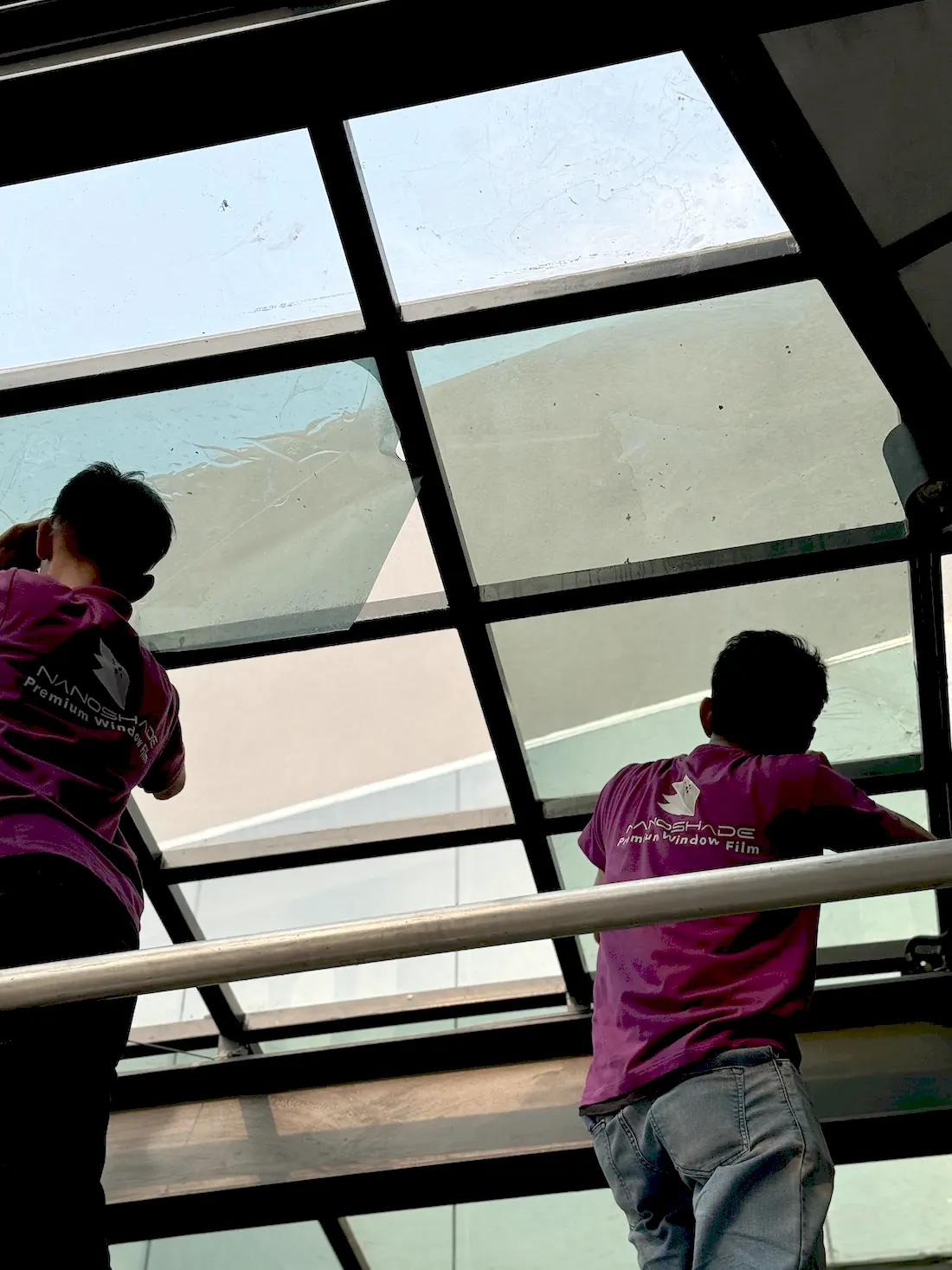 Dua teknisi NanoShade memasang film pada kaca kanopi di atas kepala di TopGolf Fatmawati Jakarta
